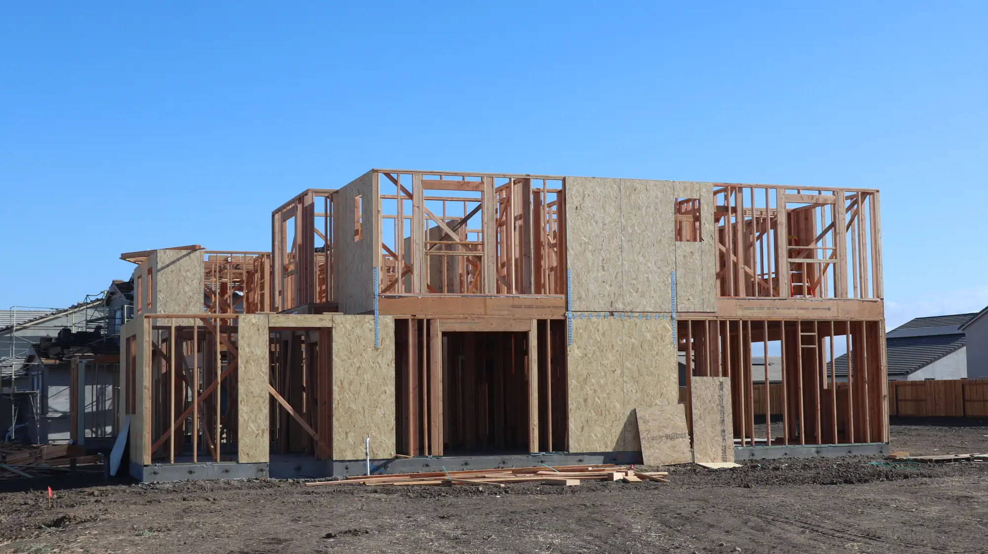 Timber framing and sheathing of a two-story house going up on a cleared lot